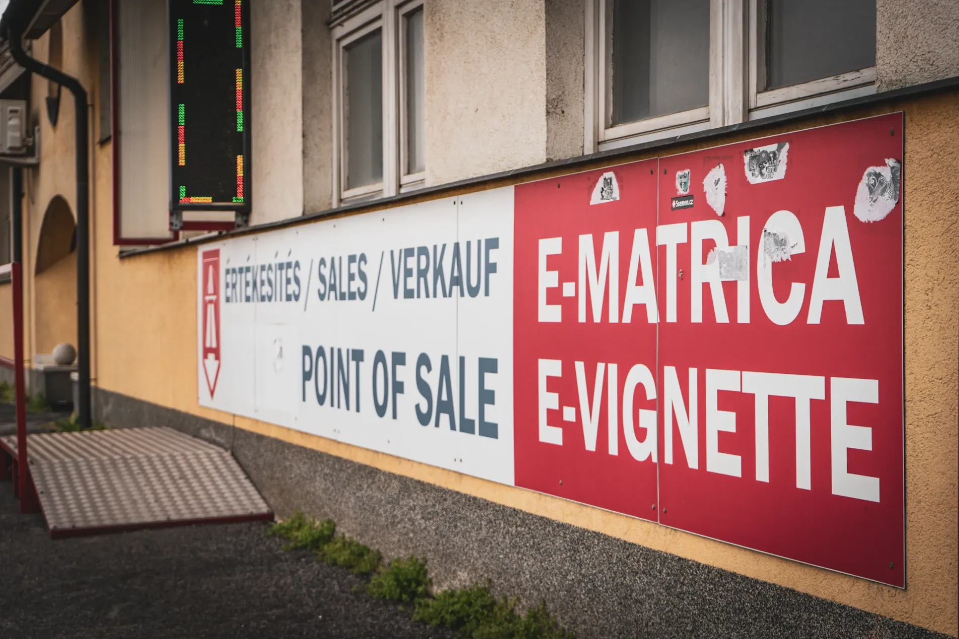 Red and white wall sign advertising Hungary E-Matrica e-vignette sales and point of sale in Hungarian, English and German