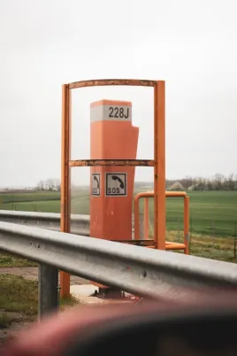 Orange Hungary motorway SOS emergency telephone post number 228J with dual SOS phone symbols on guardrail with green fields in background